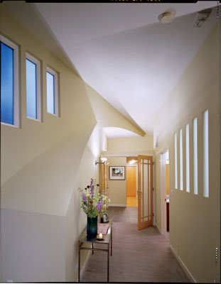 
Nestled under a curved roof, the bedroom hallway receives sunlight through the vertical windows on the left. The small windows to the right allow natural light to filter into the tub area of the master bathroom.
